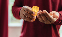 hands holding a pill bottle and getting a pill out
