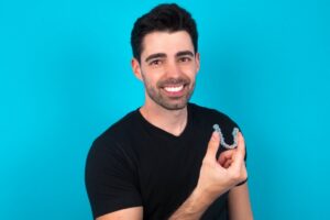 man smiling and holding an Invisalign aligner with a blue background